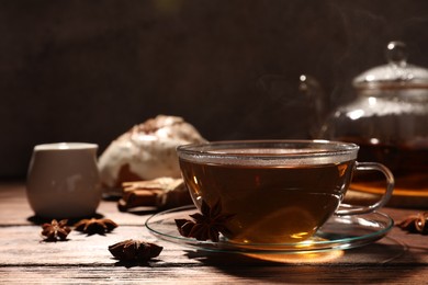 Photo of Glass cup of aromatic hot tea with anise stars on wooden table. Space for text