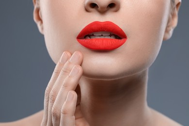 Young woman with beautiful red lips on grey background, closeup
