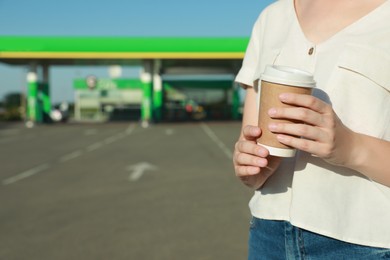 Young woman with coffee at gas station, closeup. Space for text
