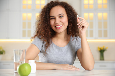 Photo of African-American woman with vitamin pill in kitchen