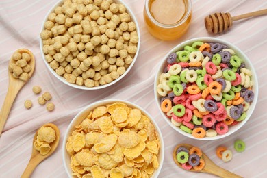 Different breakfast cereals and honey on napkin, flat lay
