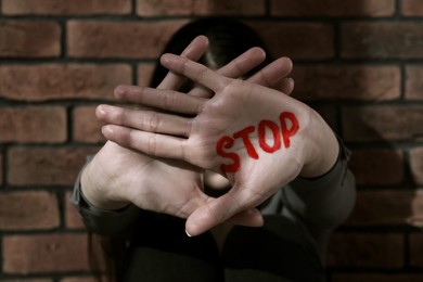 Photo of Domestic violence concept. Woman hiding her face, focus on hands with written word Stop