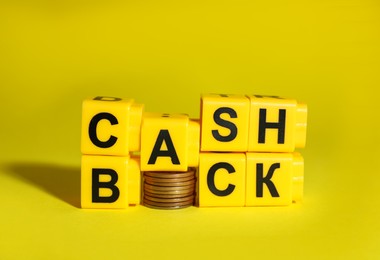 Word Cashback made with cubes and coins on yellow background, closeup