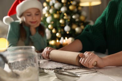 Mother teaching her daughter how to make Christmas cookies at table indoors, closeup