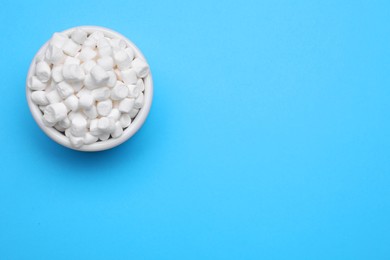 Photo of Bowl of sweet marshmallows on light blue background, top view. Space for text