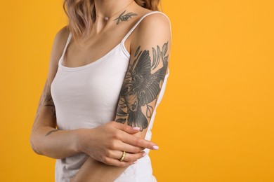 Beautiful woman with tattoos on body against yellow background, closeup. Space for text