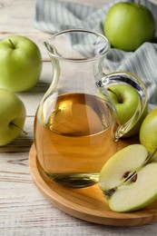 Jug of tasty juice and fresh ripe green apples on white wooden table