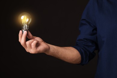 Glow up your ideas. Closeup view of man holding light bulb on black background