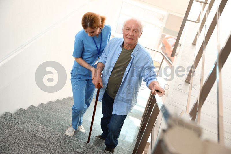 Nurse assisting elderly man on stairs indoors