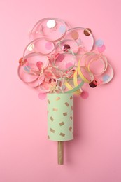 Photo of Beautiful serpentine and confetti bursting out of party popper on pink background, flat lay