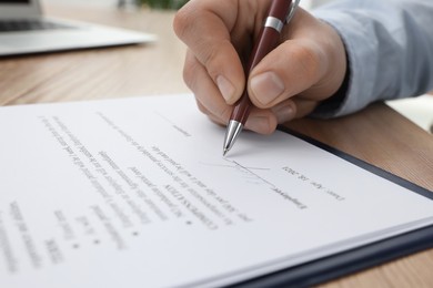 Man signing contract at wooden table, closeup
