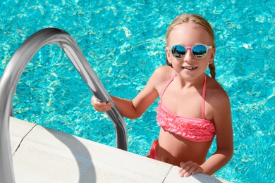 Cute little girl with sunglasses on ladder in swimming pool