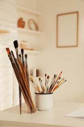 Holders with different paintbrushes on white table in studio. Artist's workplace