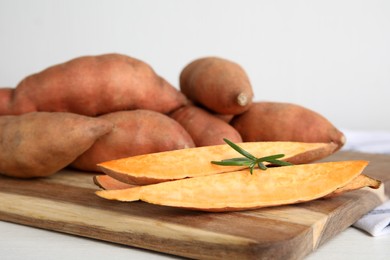 Wooden board with cut and whole sweet potatoes on white table, closeup