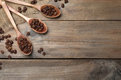 Spoons with roasted coffee beans on wooden table, flat lay. Space for text