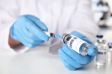 Doctor filling syringe with vaccine against Covid-19 at table, closeup