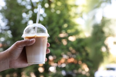 Man holding plastic takeaway cup of delicious iced coffee outdoors, closeup. Space for text