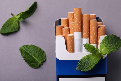 Pack of menthol cigarettes and mint leaves on grey background, flat lay