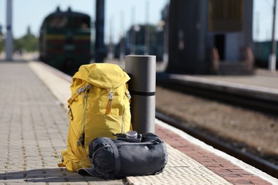 Stylish backpack, sleeping bag, camera and camping mat on railway platform outdoors. Tourism concept