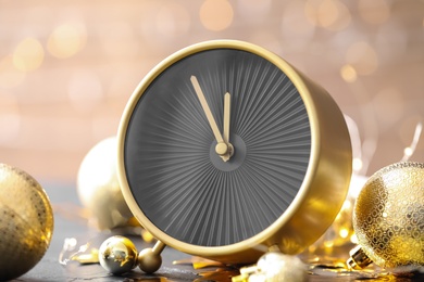 Stylish clock with decor on black table against blurred Christmas lights, closeup. New Year countdown