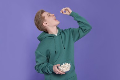 Photo of Teenage boy eating delicious popcorn on purple background