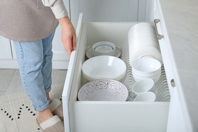 Photo of Woman opening drawer with plates and bowls in kitchen, closeup