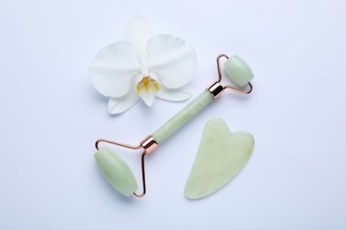 Gua sha stone, face roller and orchid flower on white background, flat lay