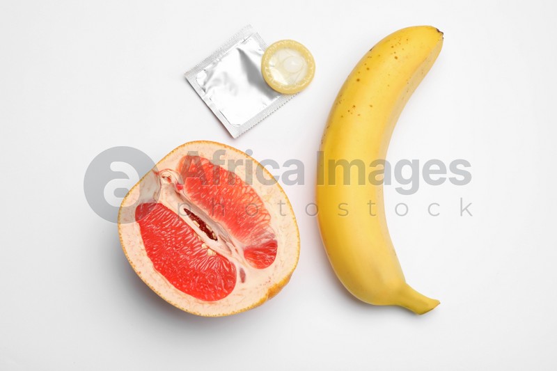 Condom, cut grapefruit and banana on white background, top view. Safe sex