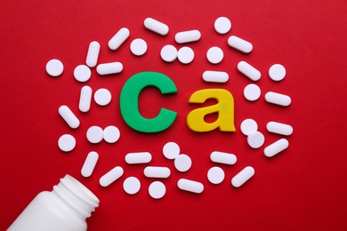 Pills, open bottle and calcium symbol made of colorful letters on red background, flat lay