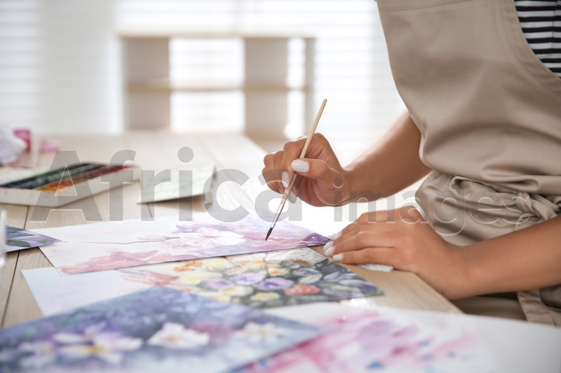 Young woman drawing flowers at table indoors, closeup. Space for text