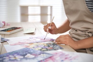 Young woman drawing flowers at table indoors, closeup. Space for text
