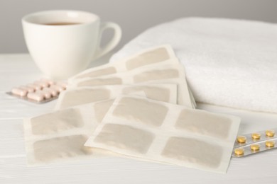 Mustard plasters, pills, towel and tea on white wooden table, closeup