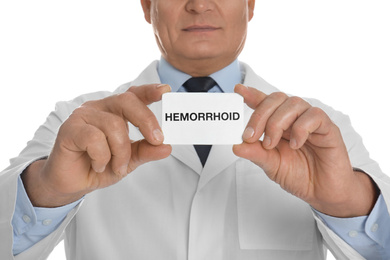 Doctor holding business card with word HEMORRHOID on white background, closeup