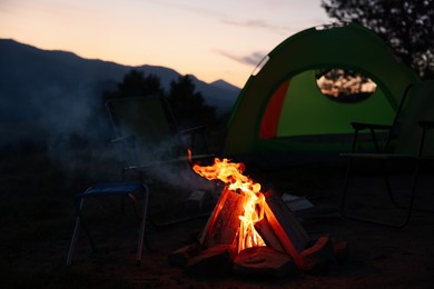 Beautiful bonfire and folding chairs near camping tent outdoors in evening