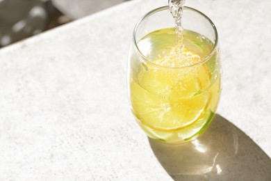 Pouring water into glass with lemon slices at light grey table, closeup. Space for text