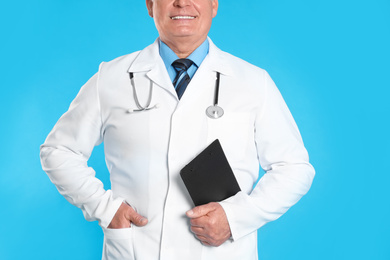 Senior doctor with clipboard on light blue background, closeup