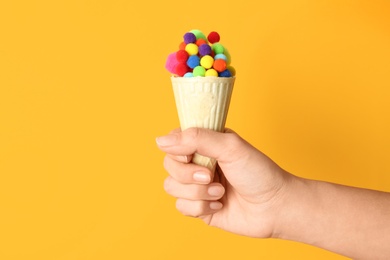Woman holding ice cream waffle with fluffy balls on yellow background, closeup