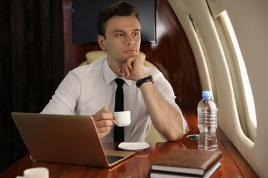 Businessman with cup of coffee looking out window in airplane during flight
