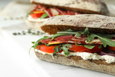 Photo of Delicious sandwiches with fresh vegetables and prosciutto on white table, closeup