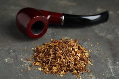 Pile of tobacco and smoking pipe on grey table