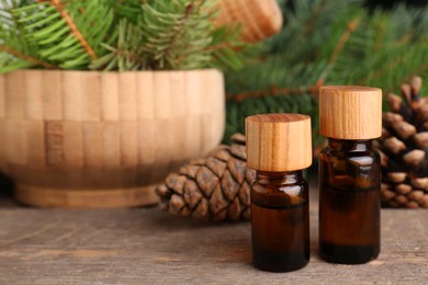 Bottles of pine essential oil, conifer tree branches and cones on wooden table. Space for text