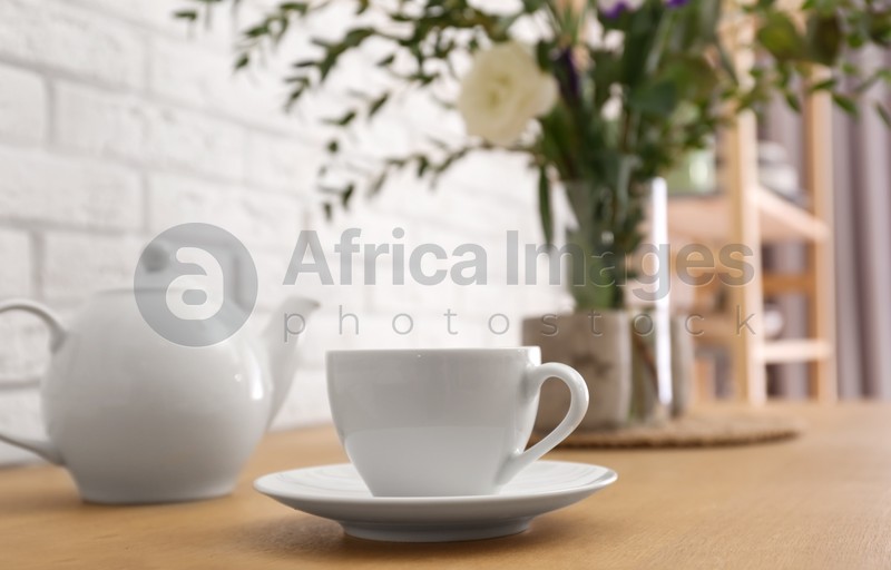 Photo of Teapot, cup and flowers on wooden dining table indoors. Kitchen interior
