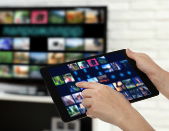 Image of Streaming video services. Woman using tablet to change channels on TV, closeup