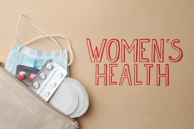 Bag with facial mask, pills and sanitary pads near words Women's Heath on beige background, top view