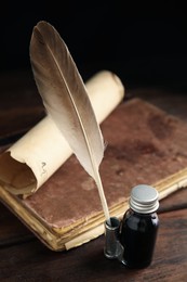 Feather pen, bottle of ink, old book and parchment scroll on wooden table