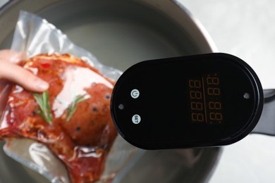 Woman putting vacuum packed meat into pot with thermal immersion circulator, closeup. Sous vide cooking