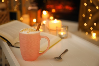 Cup of cocoa, spoon and book on white table indoors