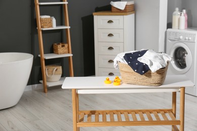 Photo of Laundry basket with baby clothes and rubber ducks on table in bathroom. Space for text