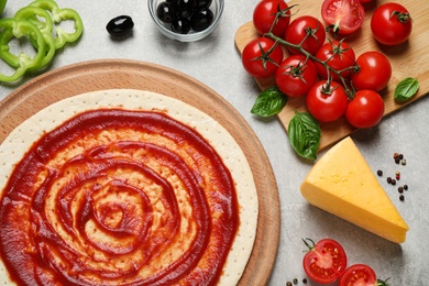 Flat lay composition with pizza crust and ingredients on grey table, closeup