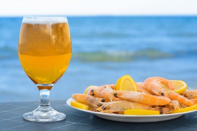 Photo of Cold beer in glass and shrimps served with lemon on beach